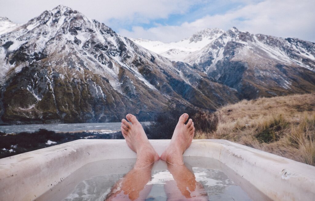 Man taking cold plunge bath outside while facing snowy mountain range